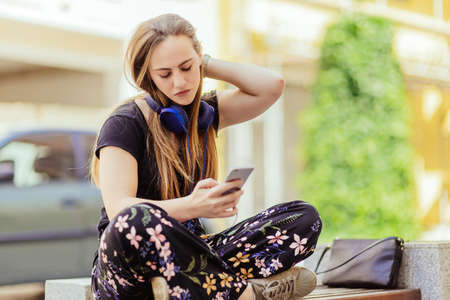 Gorgeous young blonde listenin to music in headphones while sitting on the benchの写真素材