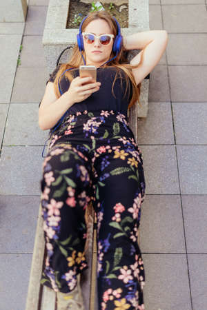 Closeup view of young girl relaxing with music on headphones while lying on the benchの写真素材