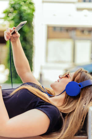 Portrait of young beautiful happy woman lying on bench and listening to musicの写真素材