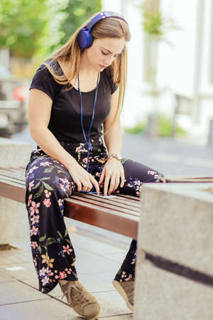 Urban girl listening to music streaming with headphones in summer whle siiting on the benchの写真素材