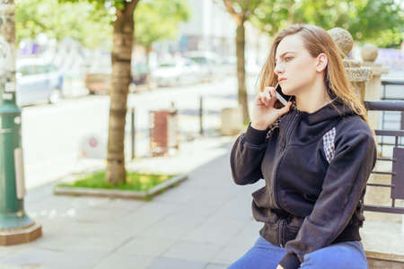 Portrait of young woman talking on mobile at street in summer timeの写真素材
