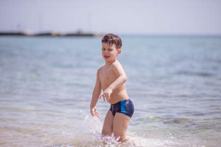 Adorable boy standing in the water on the beach playing with colorful ball and having funの写真素材