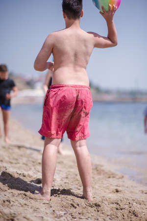 Young kid wearing red swimsuit playing with ball on the beach in the sunの写真素材