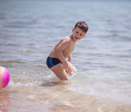 Adorable boy standing in the water on the beach playing with colorful ball and having funの写真素材