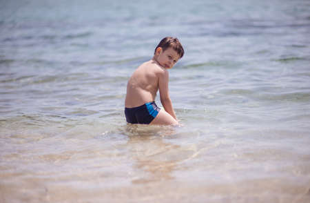 Adorable boy standing in the water on the beach playing with colorful ball and having funの写真素材