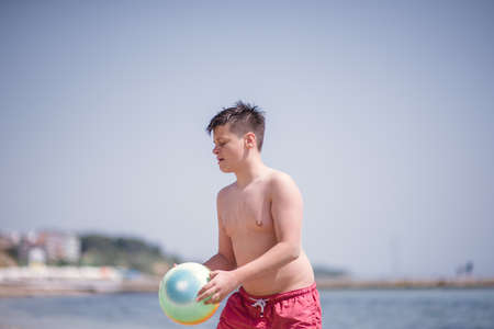 Young kid wearing red swimsuit playing with ball on the beach in the sunの写真素材