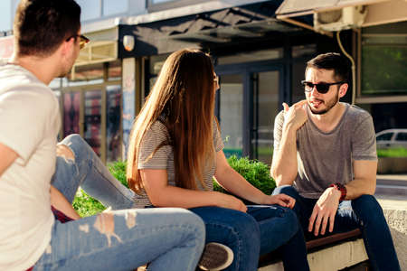 Positive three friends is talking while siiting on the bench