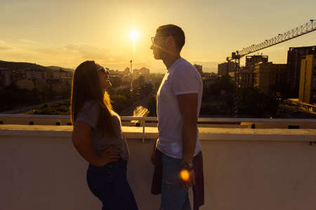 Portrait of two adult friends standing on the terrace of the top on the building on sunsetの写真素材