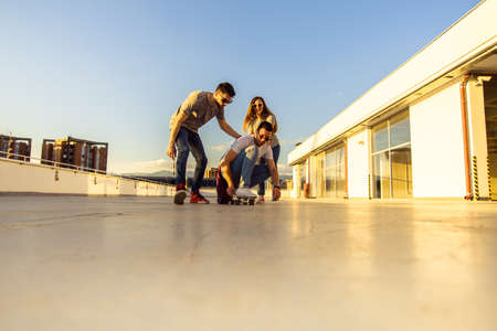 Portrait of urban friends having fun with longboard on the balcony at sunset