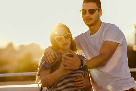 Cute couple using smartphone together on balcony at sunsetの写真素材