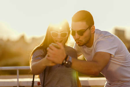 Portrait of couple of teenagers watching media content in a smart phone outdoorsの写真素材