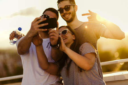 Friends having fun while taking selfie with mobile phone on balconyの写真素材