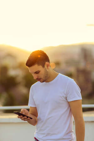 Teenager standing on the balcony on sunset and texting on his mobile phoneの写真素材