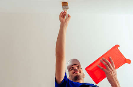 Cheerful painter in blue overall renovate his room while painting wallの写真素材