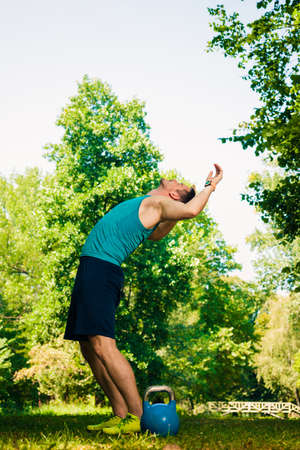 Fit man warming up before start to exercise with kettlebell into the park
