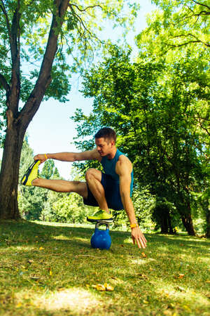 Sportive man stretching his legs on kettlebell in natureの写真素材