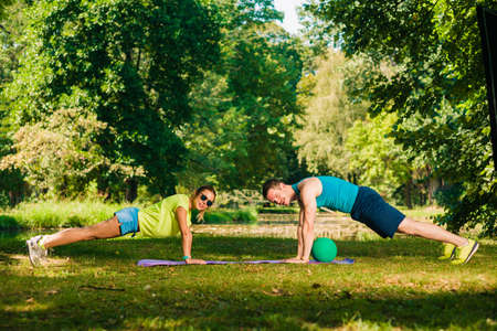 Athletic couple training push ups on the grass in the park