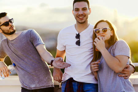Picture of three posing friends while hugging on the rooftop on the building at sunset