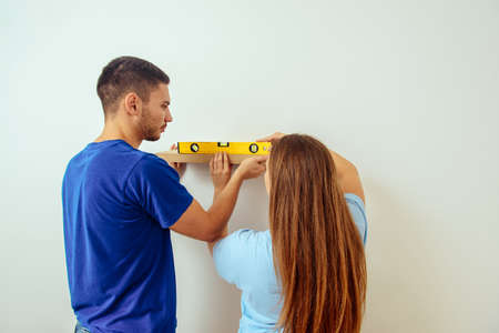 Young married couple putting shelf on the wall in their new homeの写真素材