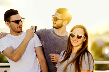 Three cheerful friends taking photos with smartphone on terrace
