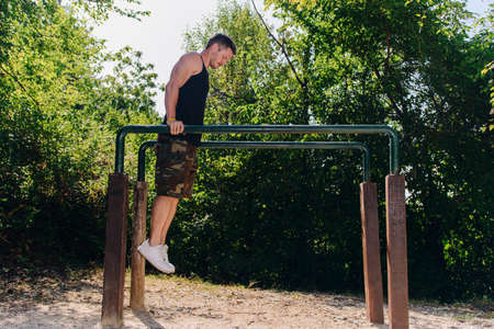 Sportive guy doing street workout on metal bars in the forest gymの写真素材