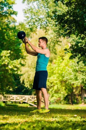 Young sportive man lifting kettlebell in the parkの写真素材