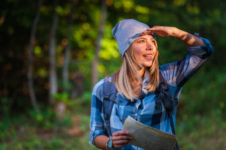 Young woman walking alone in the woods holding a map. Hiking concept in the mountain in summer