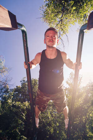 Sportive guy doing street workout on metal bars in the forest gymの写真素材