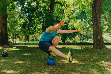 Fit man training his legs while standing on kettlebell in the park