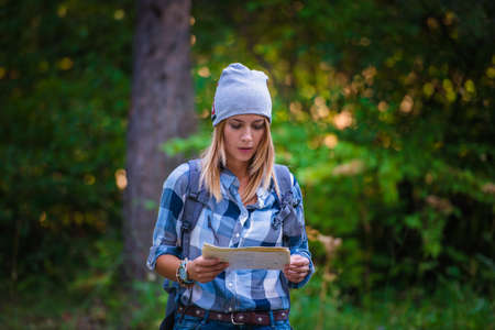 Young woman walking alone in the woods holding a map. Hiking concept in the mountain in summerの写真素材