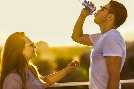 Handsome man drink water from bottle while standing with her girlfriendの写真素材