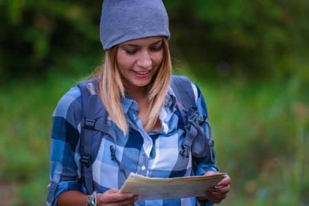 Young woman walking alone in the woods holding a map. Hiking concept in the mountain in summerの写真素材