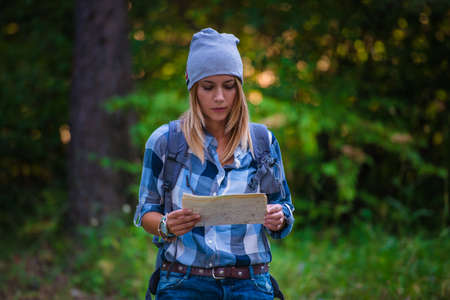 Young woman walking alone in the woods holding a map. Hiking concept in the mountain in summerの写真素材