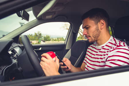 A guy in parking car is holding coffee in one hand and looking in his phoneの写真素材