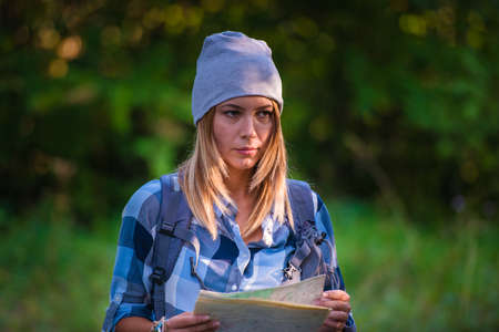 Young woman walking alone in the woods holding a map. Hiking concept in the mountain in summerの写真素材