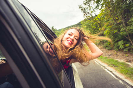 A girl is with her head out of a car window while is driving in nature, smiling and having funの写真素材