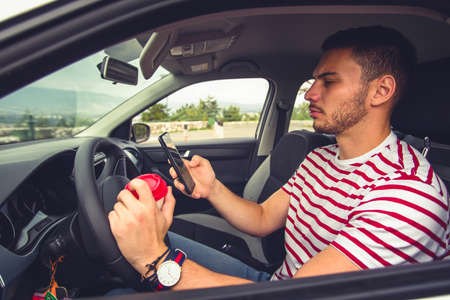 A young man is driving his car and looking curious while is having coffee and phone in his handsの写真素材