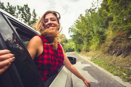 Beautiful young woman with her hand up is looking happy and relaxed while is driving in the back seatの写真素材