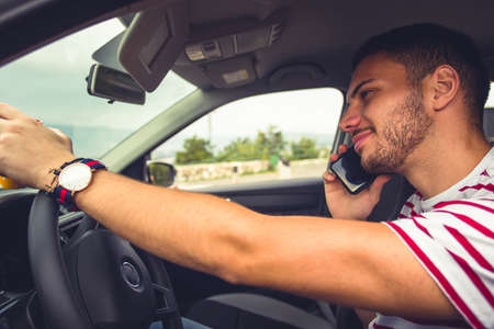 Man is driving his car, looking happy and smiling while is having conversation on his phoneの写真素材