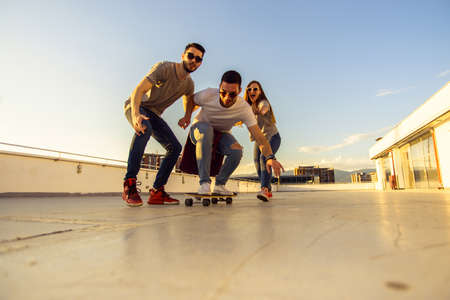Three carefree friends with longboard playing on the terrace on the rooftopの写真素材