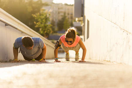 Couple in sportswear doing push-ups on the ground on urban placeの写真素材