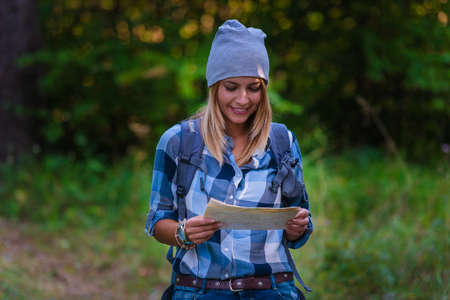 Young woman walking alone in the woods holding a map. Hiking concept in the mountain in summerの写真素材