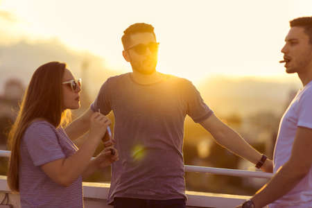 Three positive friends talking on the rooftop while eating chocoalteの写真素材