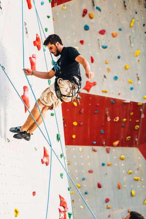 Young man descend down an outdoors artificial rock wallの写真素材