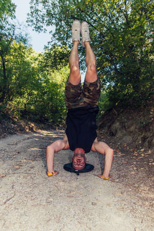 Muscles guy exercising while doing headstand on forest trailの写真素材