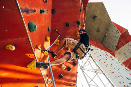 Young man climbs up an outdoors rock wallの写真素材