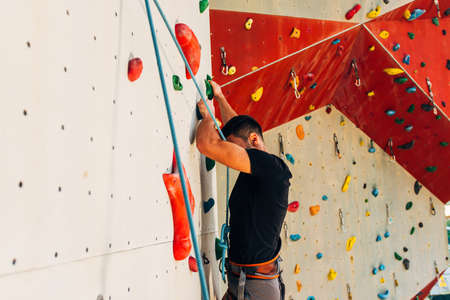 Man wearing belaying rope, climbing on a very high rock climbing wall