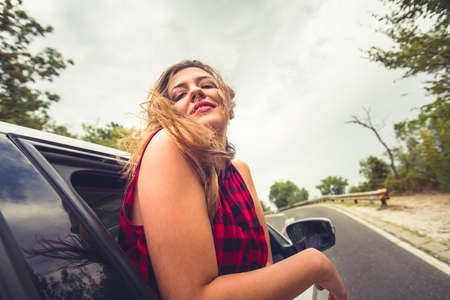 A female pulling her head out of a window while someone is driving her looking happyの写真素材