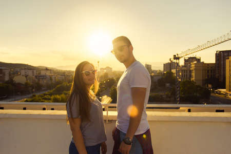 Two adult friends standing on the terrace of the top on the building on sunsetの写真素材