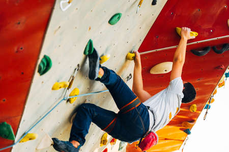 Young man climbs up an outdoors rock wallの写真素材
